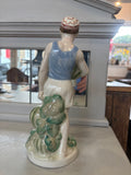 Back view of the porcelain figure showing the boy’s shirt, shorts, and foliage-style base with a second watermelon tucked into the greenery.