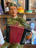 Angled view showing the soldier’s uniform, accordion, and seated pose, highlighting hand-painted detail and glossy finish.