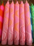 Close-up of a row of decorative candles in pink and orange with a marbled swirl pattern, neatly lined up in a basket with hints of other colourful candles at the edges.