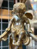 Close-up of cherub figure seated at the centre of an antique brass candelabra.