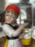 Close-up of Little Red Riding Hood’s face, showing delicate painted features and her red headscarf. She holds a yellow basket filled with goods for her grandmother.