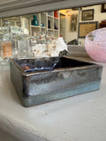 Angled side view of square pottery dish with metallic glaze finish