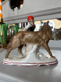 Back view of the figurine showing the Wolf’s full body and tail, and part of the girl’s headscarf and basket. The decorative tree trunk supports both figures.