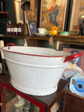 White enamel washtub with red rim and handles, vintage style.