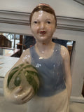 Close-up of the figurine’s face, with hand-painted details and a traditional red-patterned skullcap, cradling a green-striped watermelon.