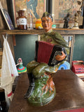 Large glazed pottery statue of a Soviet soldier in uniform seated on a tree stump, playing a red and black accordion.