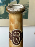 Close-up of ceramic bottle neck showing textured glaze and moulded crest medallion.