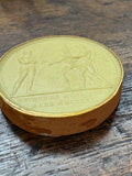 Angled view of wax medallion showing gilt edge and relief inscription