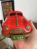 Hand holding front of Gescha R-558 red tin Porsche 356 toy car showing headlights and grille detail
