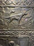 Detail of embossed brass panel showing hunting dogs in a rural landscape