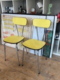 Pair of vintage yellow Formica dining chairs, three-quarter front view, chrome hairpin legs.