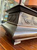 Corner of a bronze effect Crawford's casket tin showing embossed ribbon-tied fruit swags and moulded base