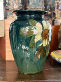 Side of an English art pottery vase showing a cream flower, green leaves and pale pink buds on a dark green ground