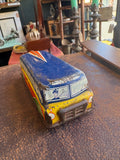 Front three-quarter view of 1950s GTP Motorways tinplate coach showing blue roof, yellow and red body with printed driver figure in windscreen and pressed metal grille at front end