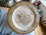 Underside of ceramic bottle showing base with worn glaze and handwritten signature.
