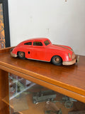 Side profile of vintage Gescha R-558 red tin friction Porsche 356 toy car on wooden shelf