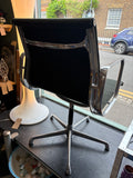 Eames EA108 chair viewed from behind, showing chrome frame, black fabric back, and swivel base.