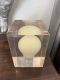 Three-quarter overhead view of Giraudon resin block showing lightbulb suspended within clear amber polyester resin.