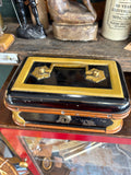 Three-quarter view of antique Victorian japanned toleware cash box showing black lacquered top with mustard yellow border, twin brass knob handles and brass keyhole escutcheon on front