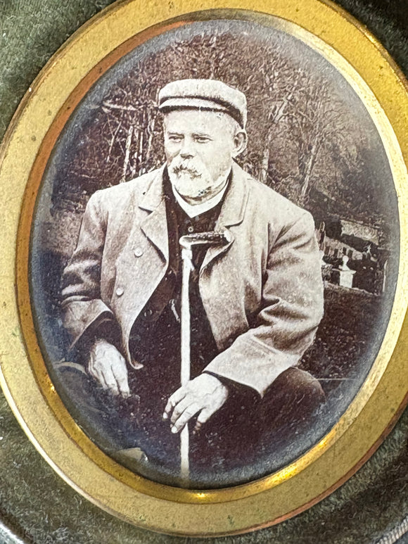 Vintage photograph of a person holding a cane, framed with gold trim.