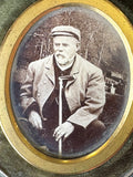 Vintage photograph of a person holding a cane, framed with gold trim.