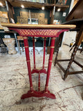 Corner detail of the red and gold painted Chinoiserie side table showing wear to the gilded edge, gilt dragonfly motif on the top surface, and the top of a faux bamboo turned leg with gold ring banding.