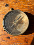 Vintage brass button compass on wooden surface. 