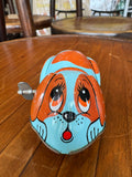 Close-up of tin wind-up dog toy's face showing painted eyes, nose, and ears in detail.