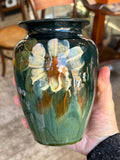 Hand-held English art pottery vase painted with a large cream flower and russet centre on a deep green glaze