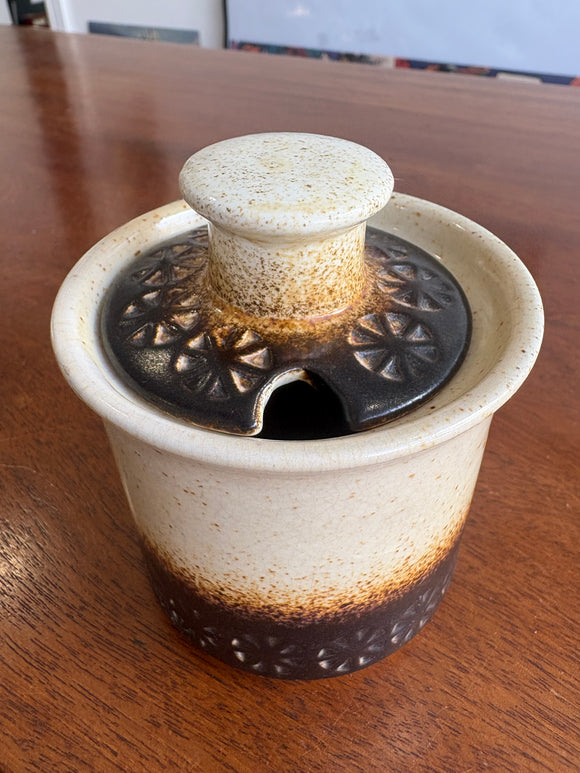 1970s Iden Pottery mustard pot with cream to brown glaze, embossed daisy motif, and matching lid. 9cm high.