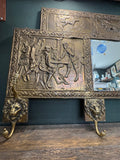 Close-up of brass repoussé panel depicting a tavern scene with lion-head hooks below