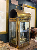 Side view of brass lantern showing domed hood, carry handle, maker's plate and bevelled glass panel