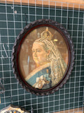 Full front view of the large oval Victorian Queen Victoria portrait in carved mahogany frame with glass, hanging on a green grid wall in an antique shop setting, showing the complete image and carved frame.