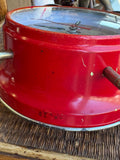 Close-up of red enamel casing showing wear, scratches and paint loss as well as partial view of two metal legs of clock 