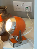 Vintage orange space age eyeball desk lamp illuminated and in use, PAT tested, shown on shelf