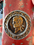 Close-up of the circular portrait medallion on the scabbard, showing a laurel-wreathed profile bust in gold and silver paint on a red ground.