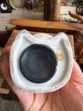 Underside of bisque pig money bank showing rubber stopper plug and shaped foot outline with partial label remnant.