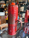 Side view of studio pottery jug showing handle and red glaze texture