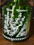 Close-up of white printed thyme and rosemary detail on green glass jar