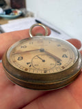 A 1940s Moeris pocket watch held in a person's hand, showing a round brass case, cream-colored dial, and black Arabic numerals.