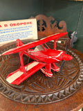 Vintage red metal Pitts Special biplane model G-PITZ front three-quarter view on carved wooden table
