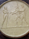 Close-up of wax medallion showing soldier figures and inscription along the base
