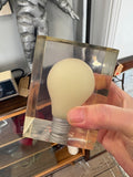 Hand holding Giraudon resin lightbulb sculpture showing scale — frosted bulb and screw base visible through clear block.