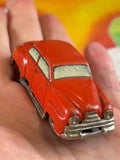 Hand holding vintage red US-Zone Germany tin litho sedan toy car showing front three-quarter detail