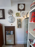 Anne Plant ceramic wall hanging displayed on wall with vintage clocks.