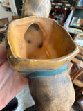 Close-up of the rim and interior of the mustard yellow saddle planter on the ceramic tiger, showing the teal blue strap band around the exterior, the glazed inner surface, and the hollow body construction below.