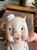 Close-up of hand-painted face of vintage bisque pig bank showing lashed eyes, red-tipped nostrils and open mouth detail.