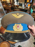 Hand holding a Soviet Air Force officer's peaked cap showing the badges, blue band and gilt cords