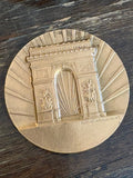 Reverse of medallion showing stylised Arc de Triomphe with starburst background