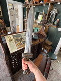 Hand holding the sword pommel to show scale, with the lion-head handle and rectangular cross-guard against a shop interior background.